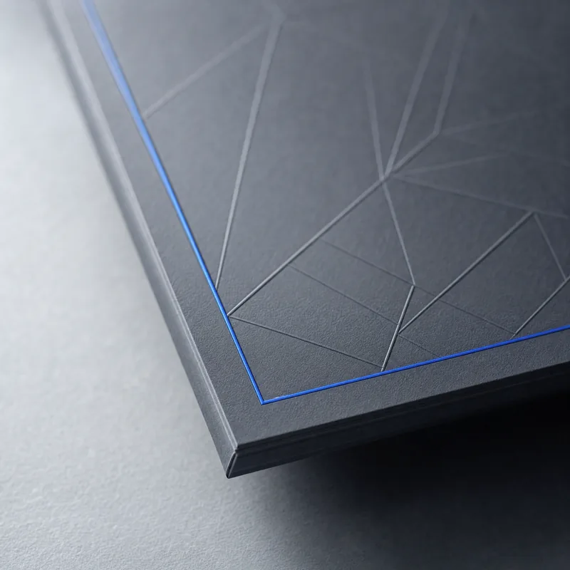 Macro of a matte slate cover with a blind-embossed pattern and a cobalt hairline along the edge.