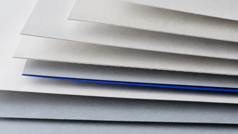 Layered paper sheets fanned in shallow steps, one thin cobalt edge among them.