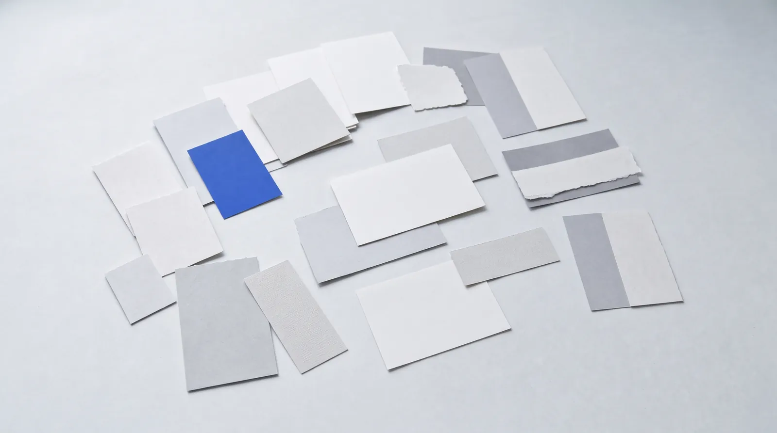 Twenty blank paper cards scattered loosely across a grey studio surface, one of them cobalt blue.